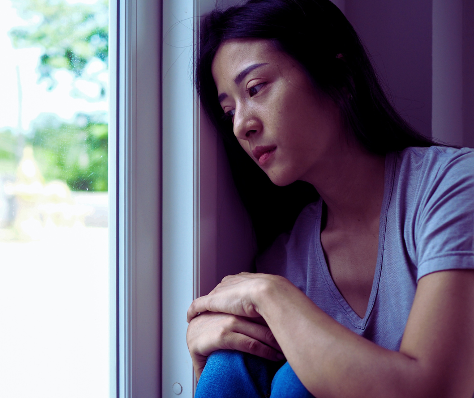 Woman with postpartum depression looking out the window and looking sad.