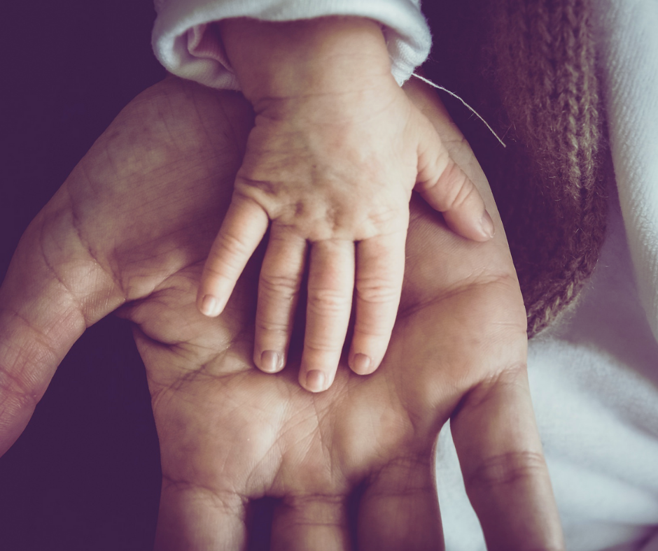 A parent holds their baby's hand as they reparent themselves
